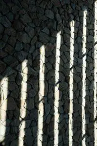 Shadows of vertical bars cast on a stone wall.